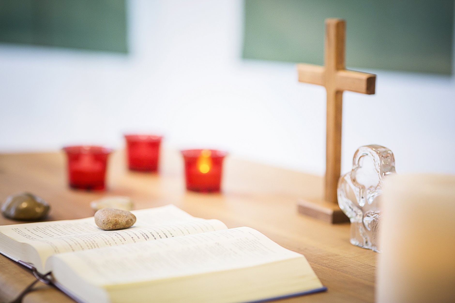 HGZ | Klinikseelsorge Dies ist eine aufgeschlagene Bibel, die vor Kerzen und einem Holzkreuz auf einem Tisch liegt.