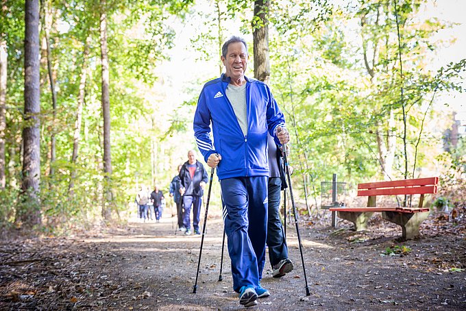 Dies sind Patienten beim Nordic Walking durch einen grün belaubten Wald.