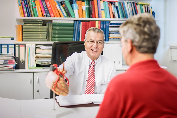 Dies ist Dr. Aiman Alken, Chefarzt der Klinik für Anästhesiologie und Intensivmedizin und stellvertretender Ärztlicher Direktor, der einem Patienten ein Herz-Modell erklärt.