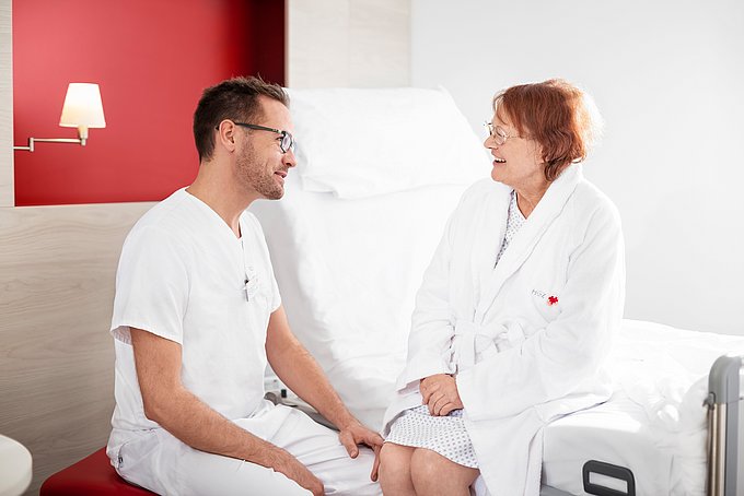 Dies ist ein Pfleger mit einer älteren Patientin im Patientenzimmer.