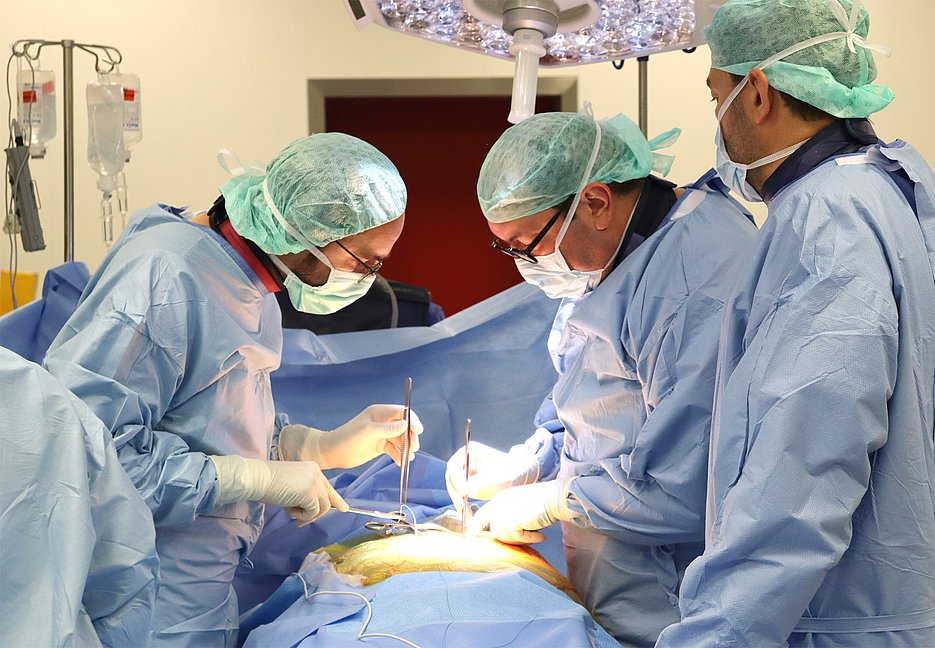 Drei Operateure stehen bei einem Eingriff am OP-Tisch.