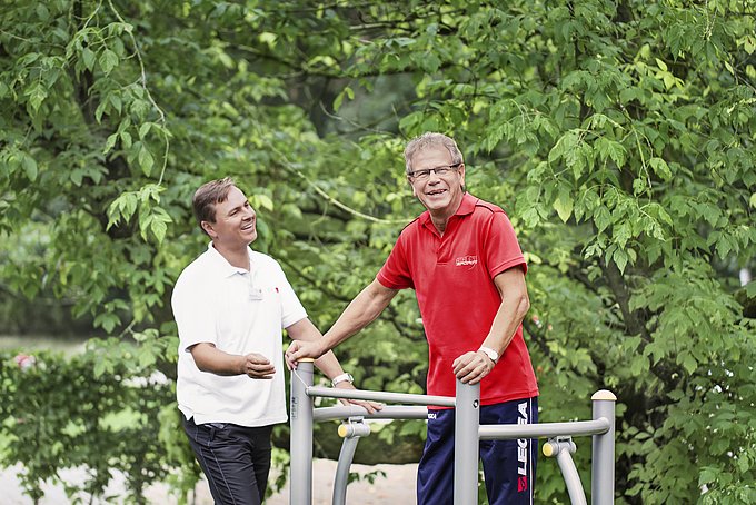 Dies sind ein Patient und die Leitung der Physikalischen Therapie, Alexander Bär, an einem Fitnessgerät im Herzgarten.