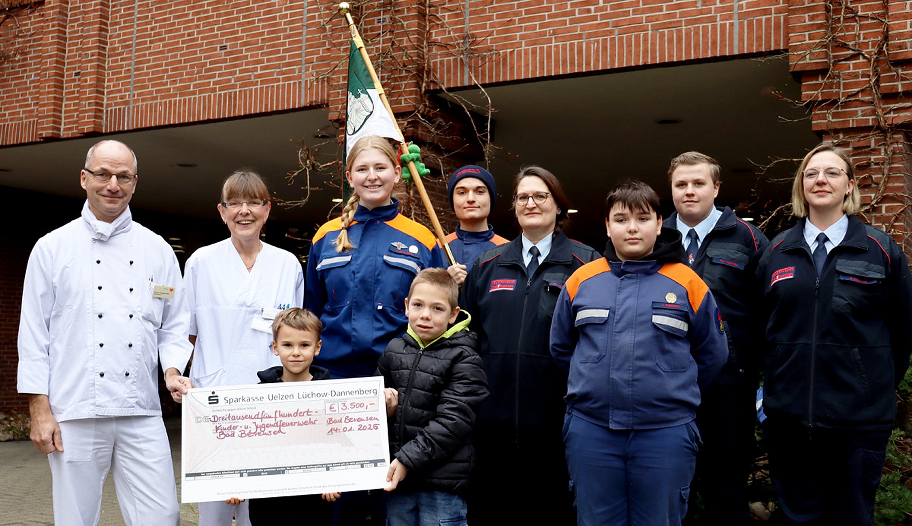 Mehrere Personen stehen beisammen, einige tragen Feuerwehr-Uniformen, zwei Kinder im Vordergrund halten einen überdimensionierten, symbolischen Scheck.